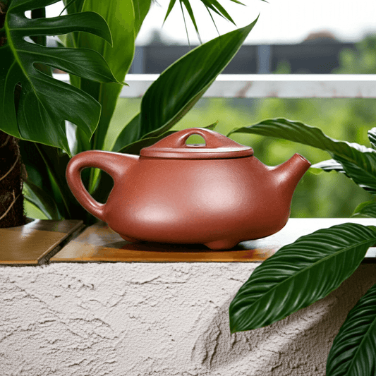 Handmade Yixing purple sand teapot, original craftsmanship, displayed among green plants, ideal for tea enthusiasts.