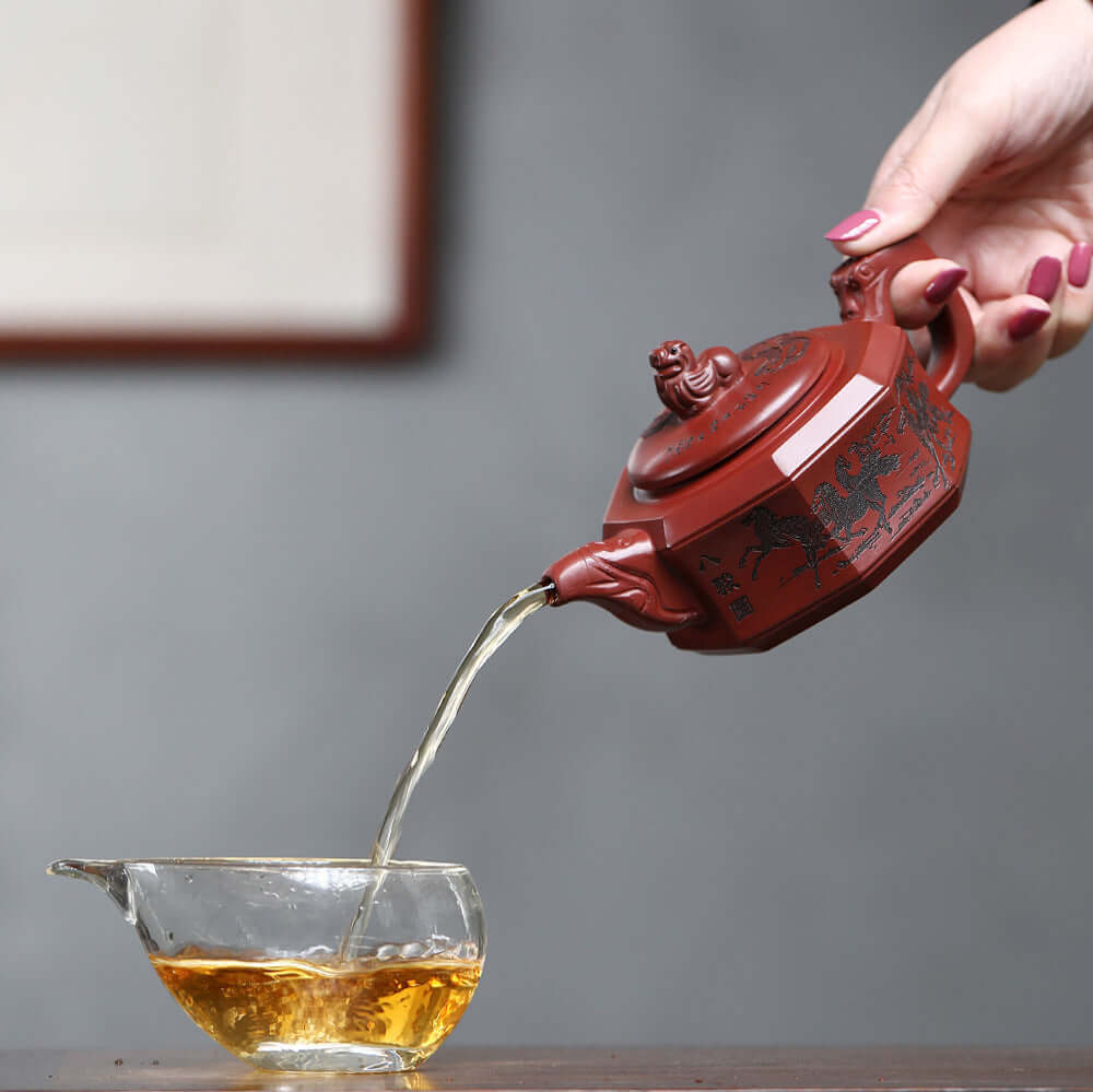 Handmade Yixing purple sand teapot pouring tea into a glass cup, showcasing elegant craftsmanship and tradition.