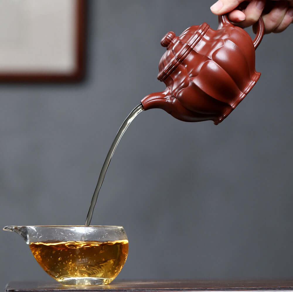 Handmade Yixing purple sand teapot pouring tea into a glass cup, showcasing craftsmanship and elegance.