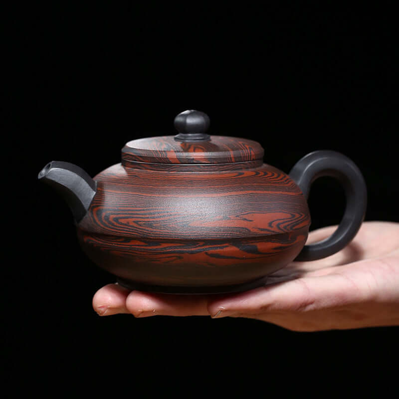 Handmade Yixing purple sand teapot in a person's hand, showcasing rich colors and elegant design.