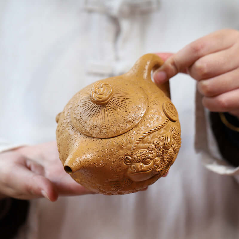 Handmade Yixing purple sand teapot featuring intricate dragon design, held by a person in traditional attire.