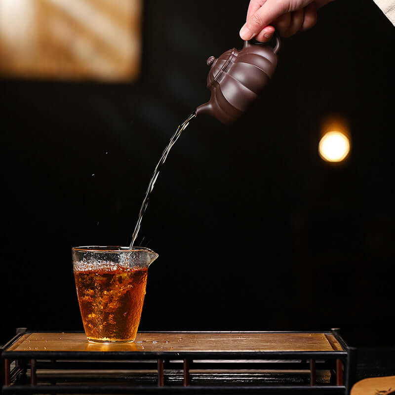 Handmade Yixing purple sand teapot pouring tea into a glass, showcasing unique craftsmanship and original materials.