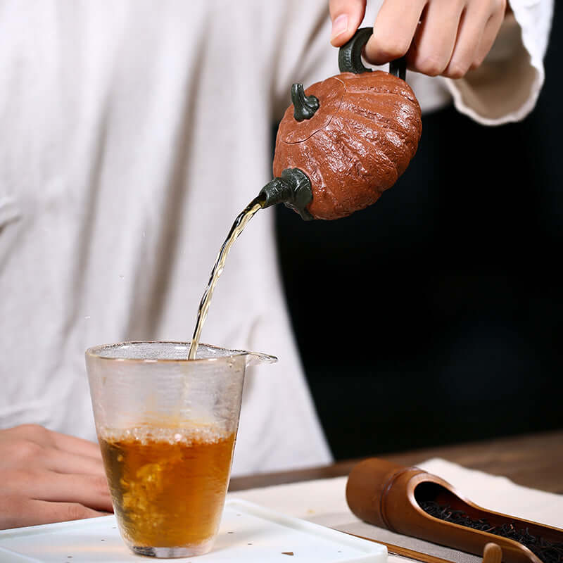 Handmade Yixing purple sand teapot pouring tea into a glass cup, showcasing unique pumpkin design and craftsmanship.