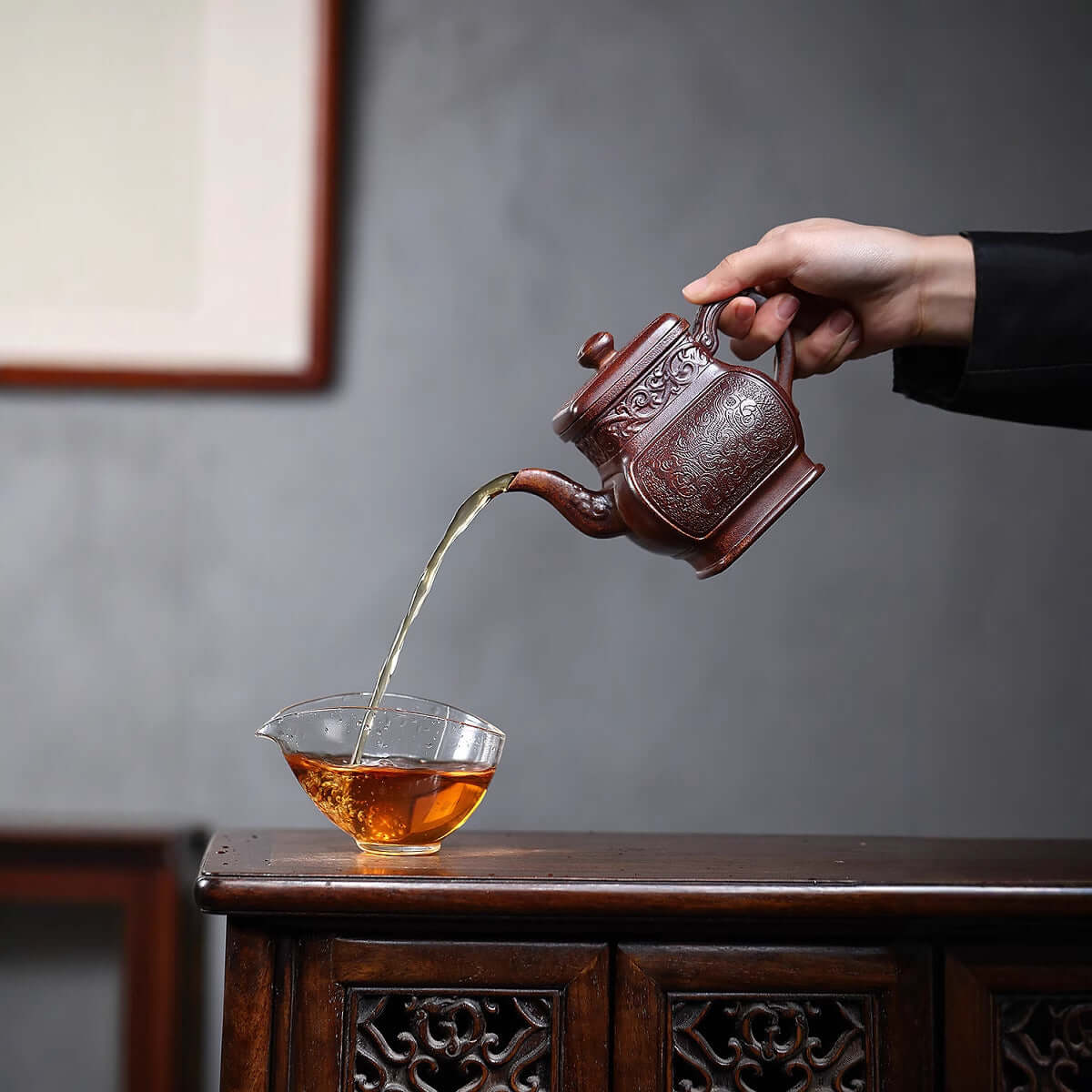 Handmade Yixing purple sand teapot pouring tea into a glass cup, showcasing artisanal craftsmanship and elegant design.