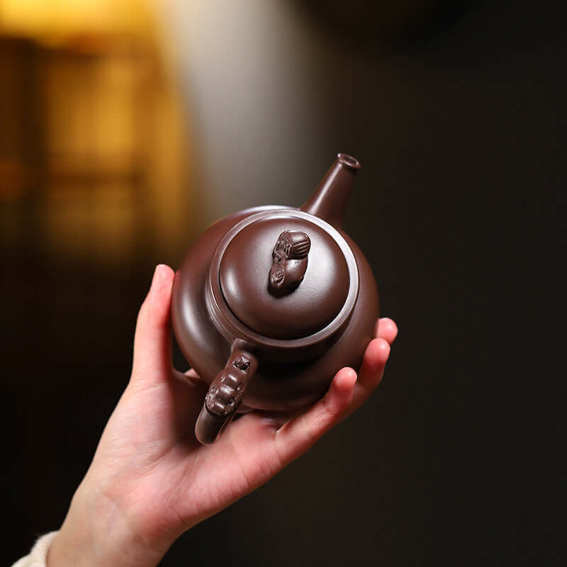 Handmade Yixing purple sand teapot held in a hand, showcasing intricate lion-shaped handle and elegant design.