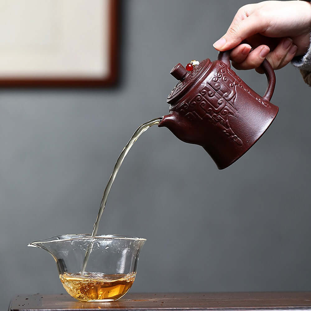Handmade Yixing purple sand teapot pouring tea into a glass cup, showcasing traditional kung fu tea set craftsmanship.