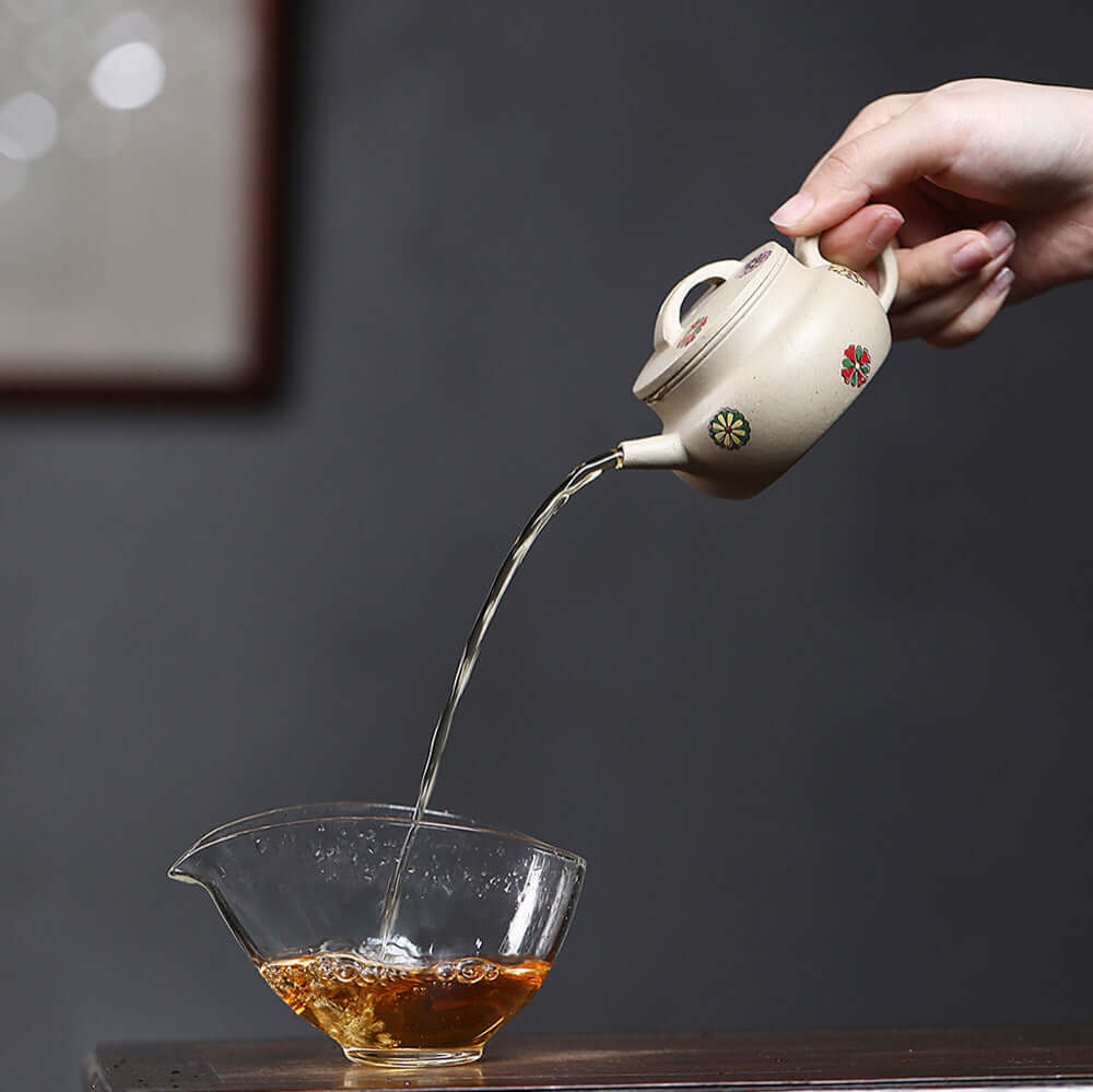 Handmade Yixing purple sand teapot pouring tea into glass cup, showcasing craftsmanship and Chinese tea culture.