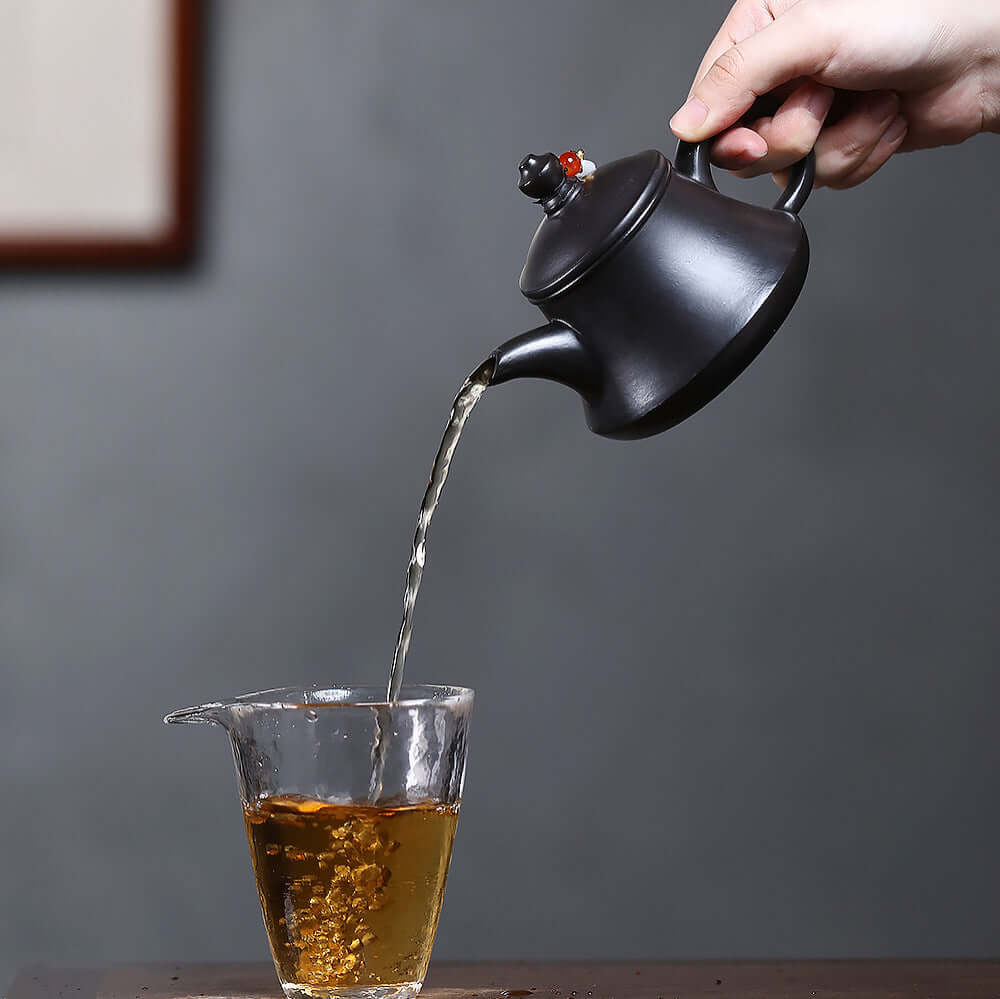 Handmade Yixing purple sand teapot pouring tea into a clear glass cup, showcasing traditional Kung Fu tea set craftsmanship.