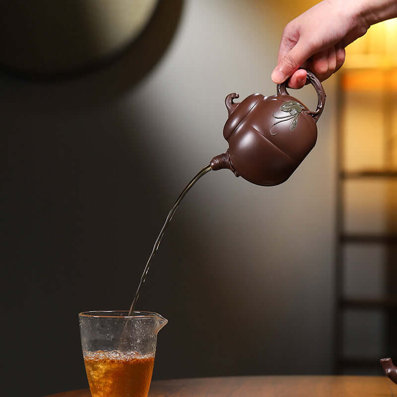 Handmade Yixing purple sand teapot pouring tea into a glass cup, showcasing elegant craftsmanship.