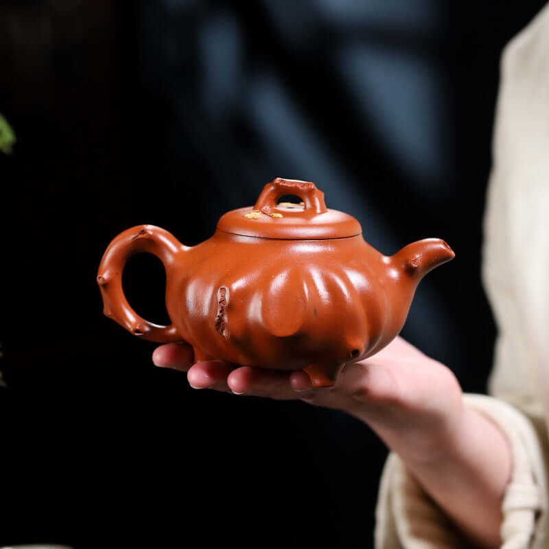 Handmade Yixing purple sand teapot held in hand, showcasing unique design and craftsmanship, perfect for tea lovers.