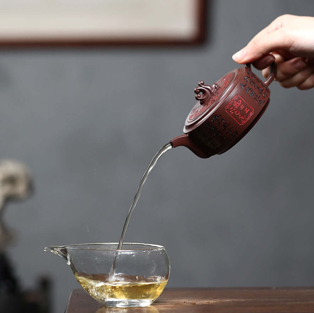 Handmade Yixing purple sand teapot pouring tea into a clear cup, showcasing traditional craftsmanship.