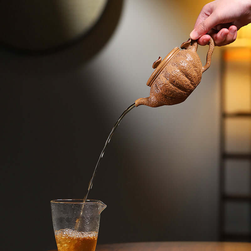 Hand pouring tea from a handmade Yixing purple sand teapot into a glass cup, showcasing traditional craftsmanship.