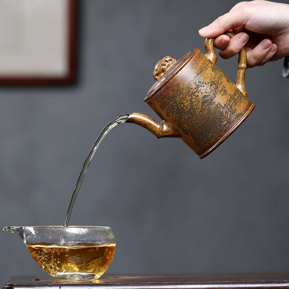 Handmade Yixing purple sand teapot pouring tea into a glass cup, showcasing unique craftsmanship and artistry.