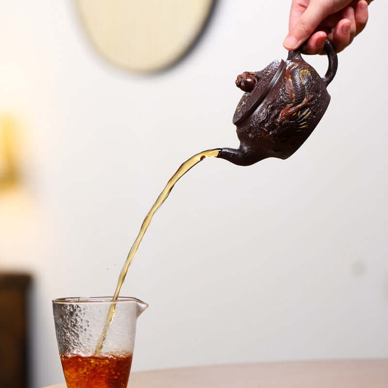 Handmade Yixing purple sand teapot pouring tea into a glass cup, showcasing traditional craft and elegance.