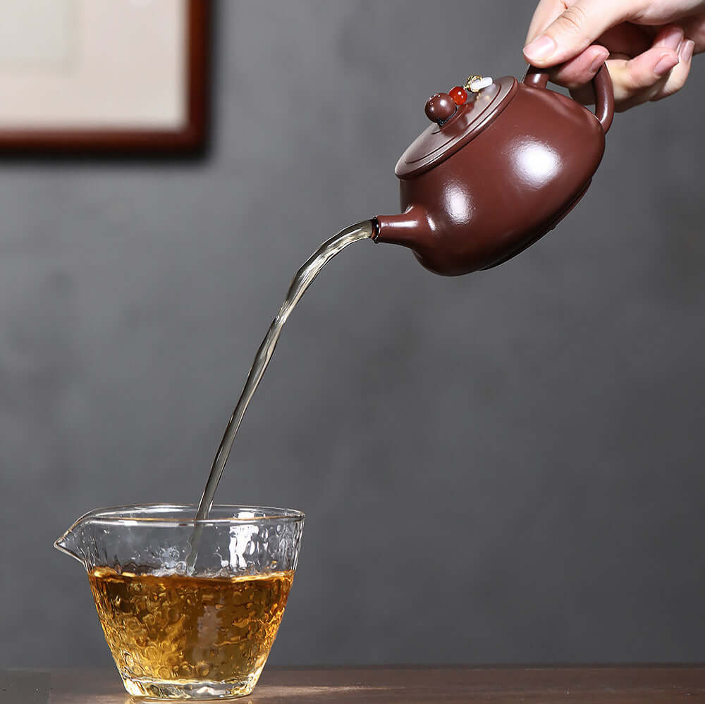 Handmade Yixing purple sand teapot pouring tea into a glass, flat lid design for Kung Fu tea set.