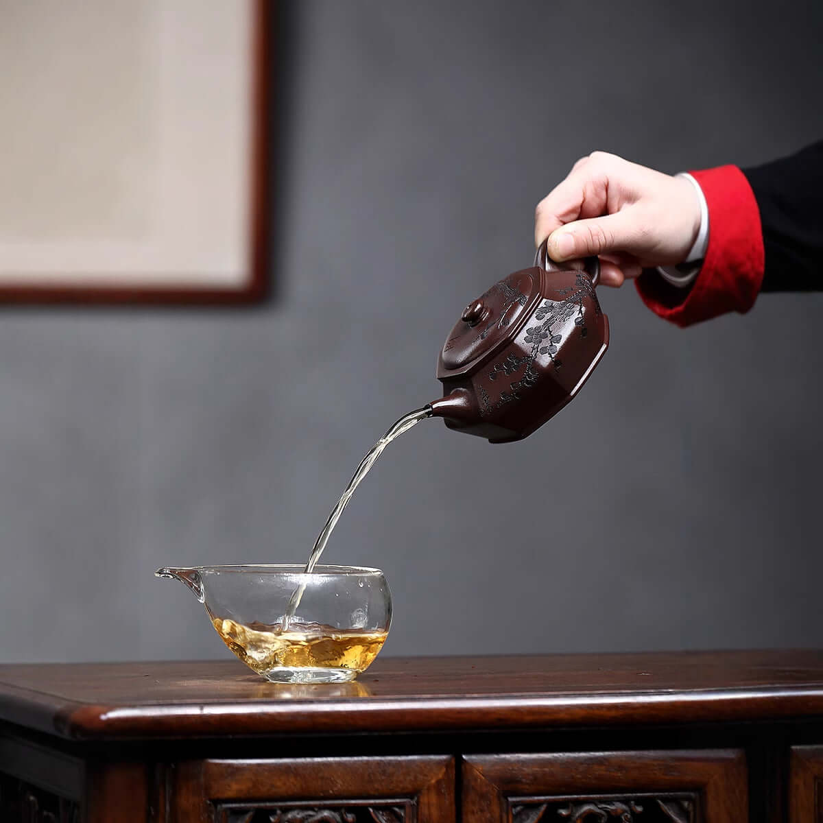 Handmade Yixing purple sand teapot pouring tea into a clear cup, showcasing traditional craftsmanship and elegance.