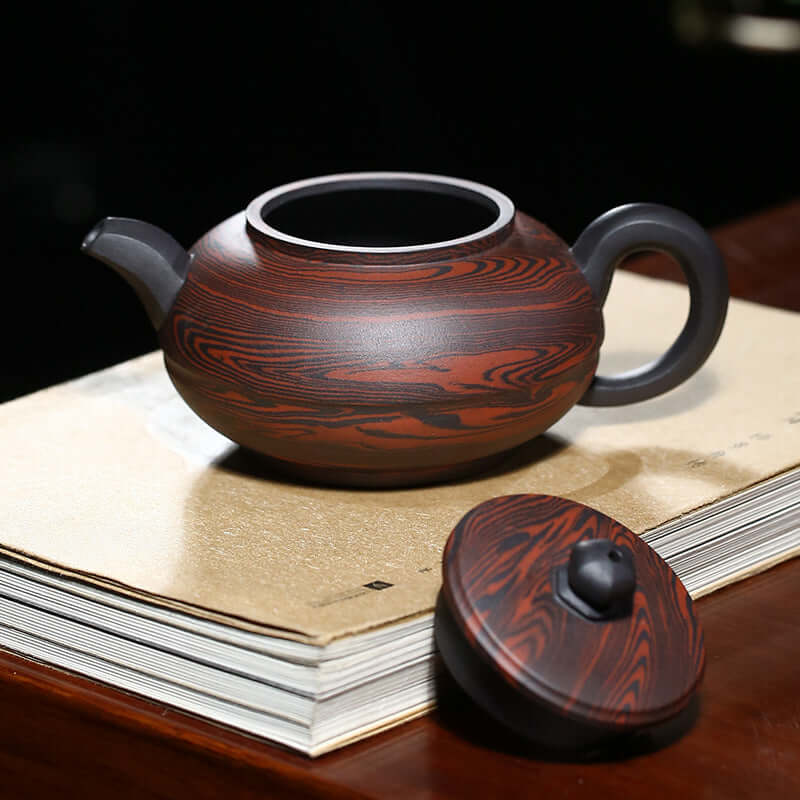 Handmade Yixing purple sand teapot with a distinctive red and black swirl design, displayed on a wooden surface.