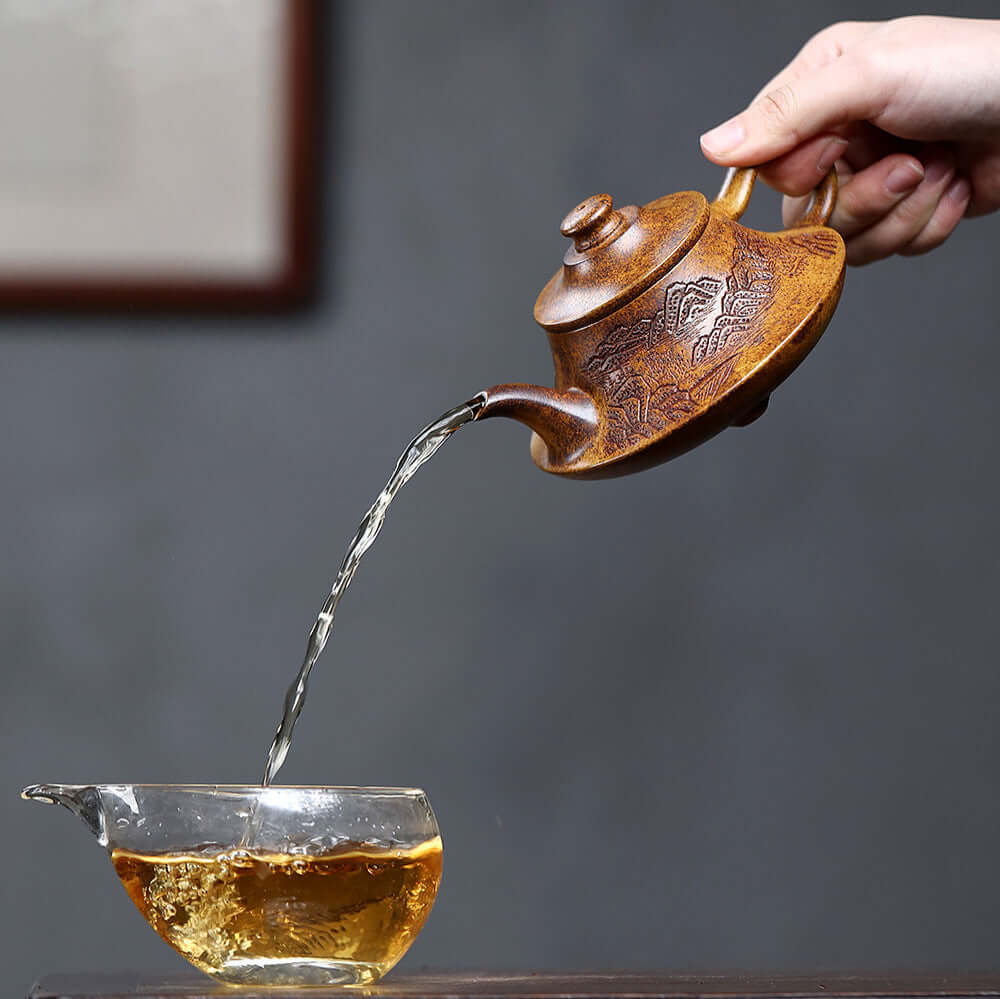 Handmade Yixing purple sand teapot pouring tea into a glass cup, showcasing unique craftsmanship and traditional design.