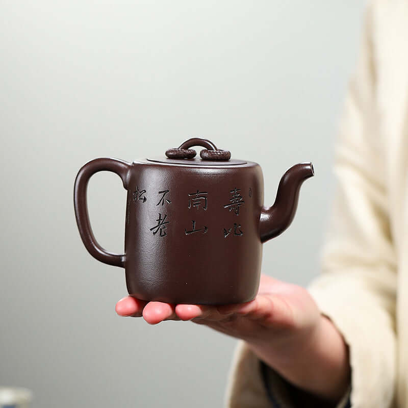 Handmade Yixing purple sand teapot held in hand, featuring intricate calligraphy and traditional design.