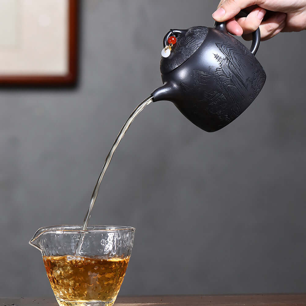 Handmade Yixing purple sand teapot pouring tea into a glass cup, showcasing original craftsmanship and design.