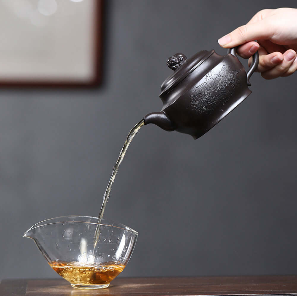 Handmade Yixing purple sand teapot pouring tea into a glass cup, showcasing craftsmanship in tea brewing.