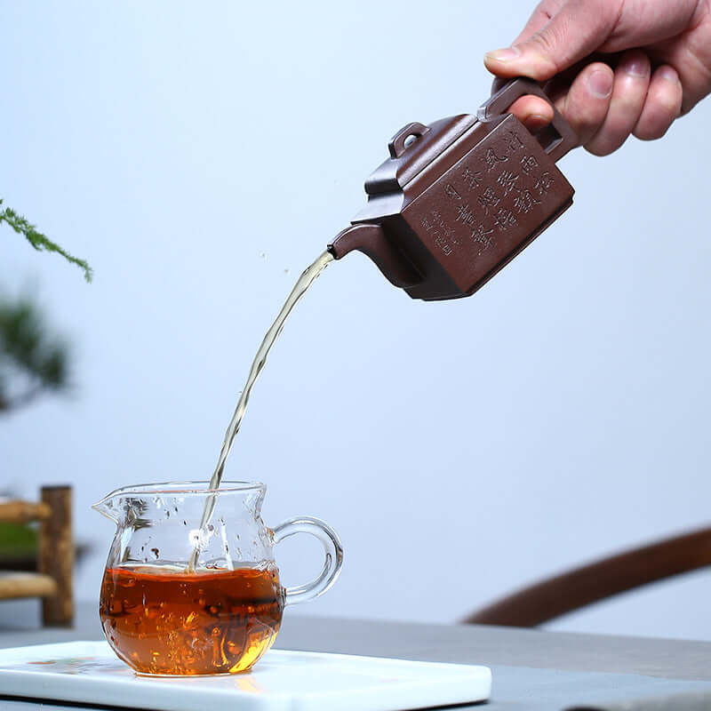 Handmade Yixing purple sand teapot pouring tea into a glass cup, showcasing traditional Chinese tea culture.