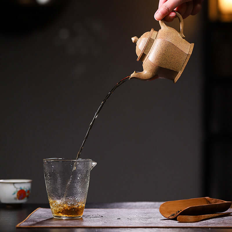 Handmade Yixing purple sand teapot pouring tea into a glass cup, showcasing high-quality craftsmanship.