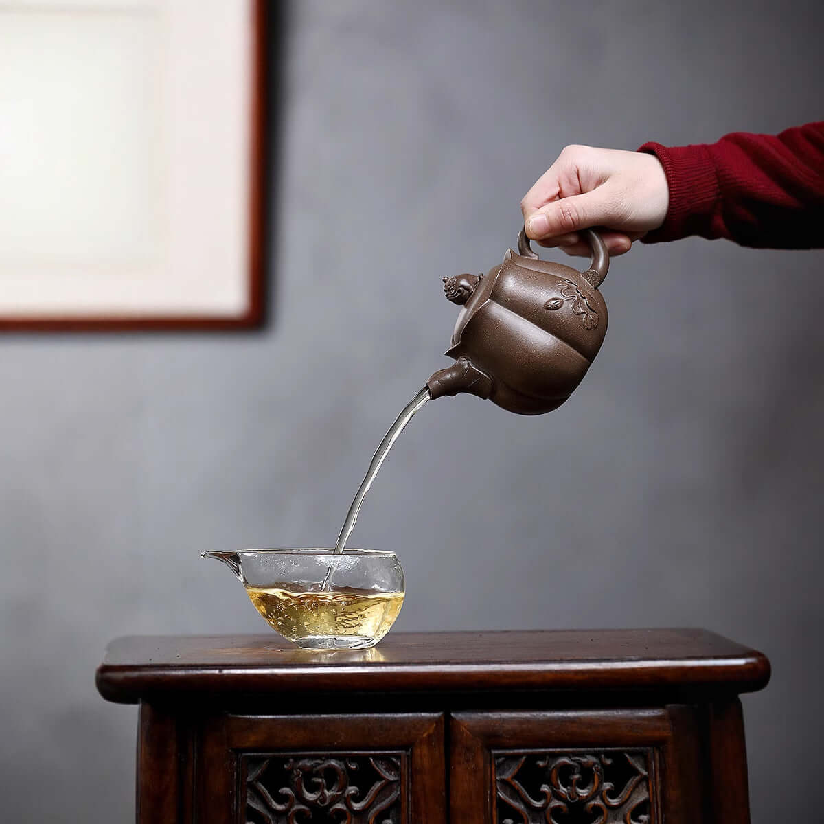 Handmade Yixing purple sand teapot pouring tea into a glass cup, showcasing traditional kung fu tea set craftsmanship.
