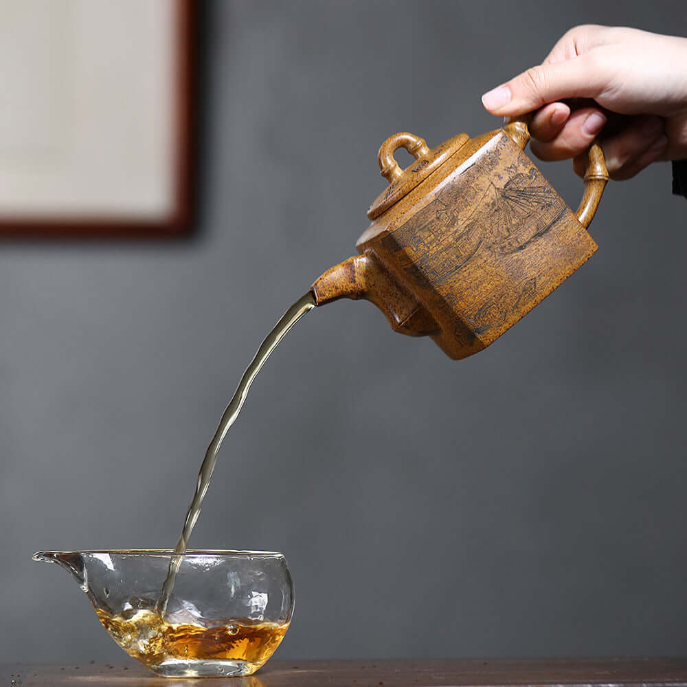Handmade Yixing purple sand teapot pouring tea into a glass cup, showcasing traditional kung fu tea ceremony.