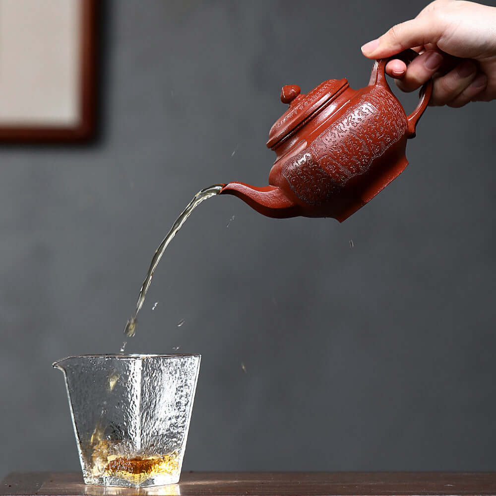 Handmade Yixing purple sand teapot pouring tea into a glass cup, showcasing traditional kung fu tea style.