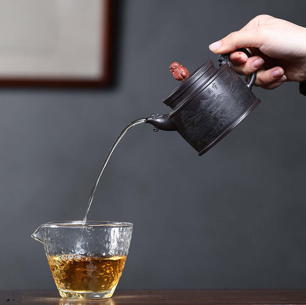Handmade Yixing purple sand teapot pouring tea into a glass cup, showcasing elegant craftsmanship and traditional design.
