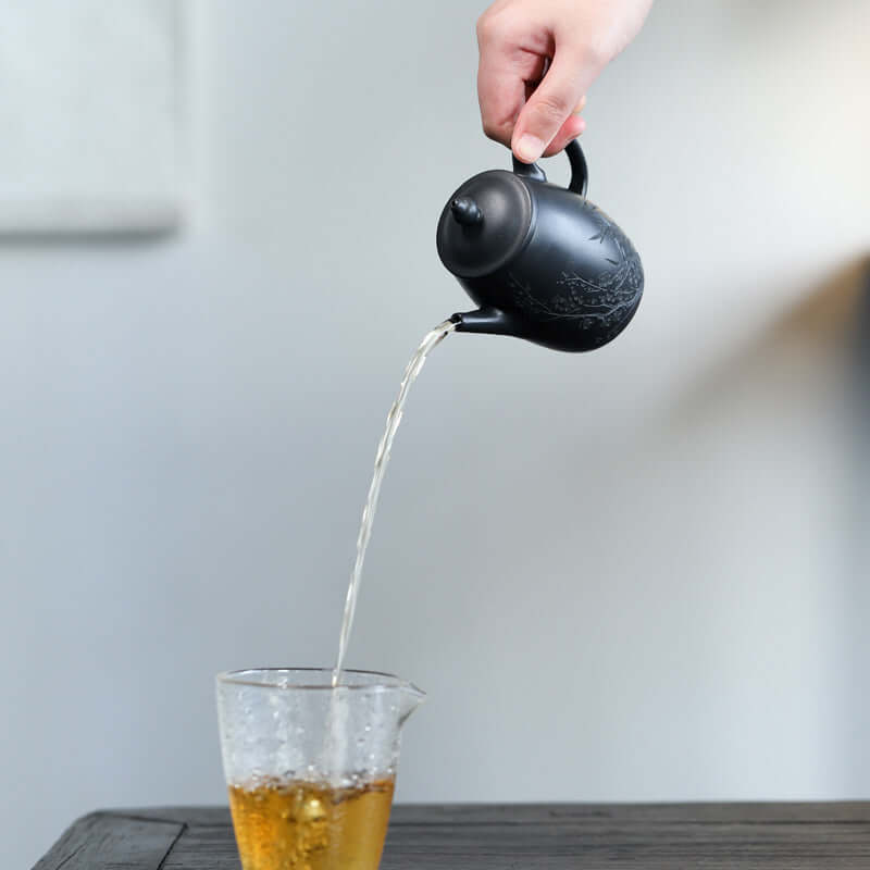 Handmade Yixing purple sand teapot pouring tea into a glass cup, showcasing elegant design and fine craftsmanship.