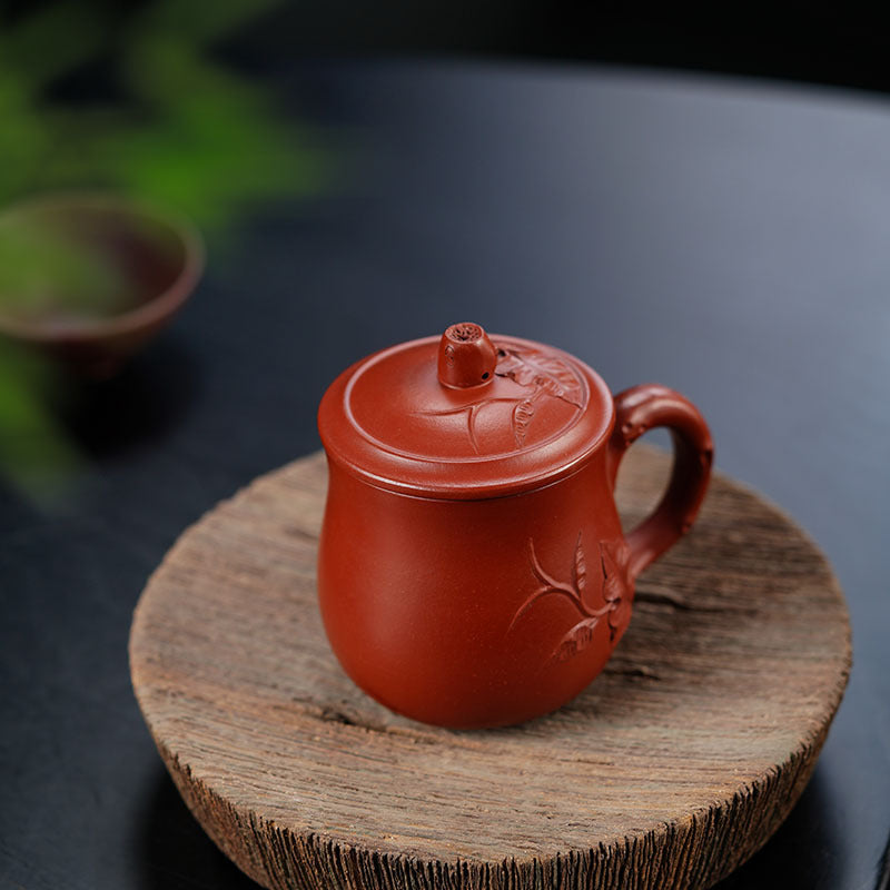 Handmade Yixing purple sand tea cup with lid, featuring intricate craftsmanship on a wooden coaster.