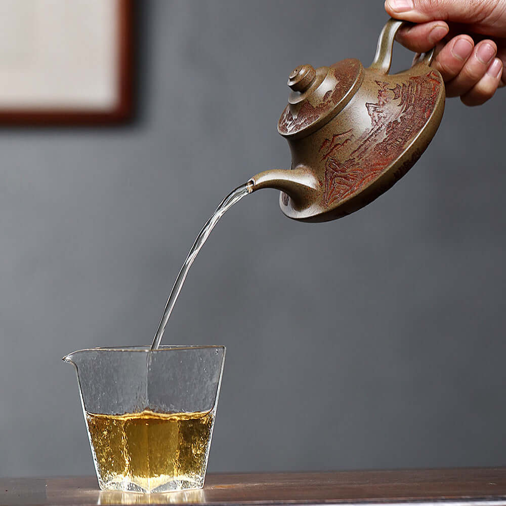 Handmade Yixing purple sand teapot pouring tea into a glass cup, showcasing craftsmanship and elegance.