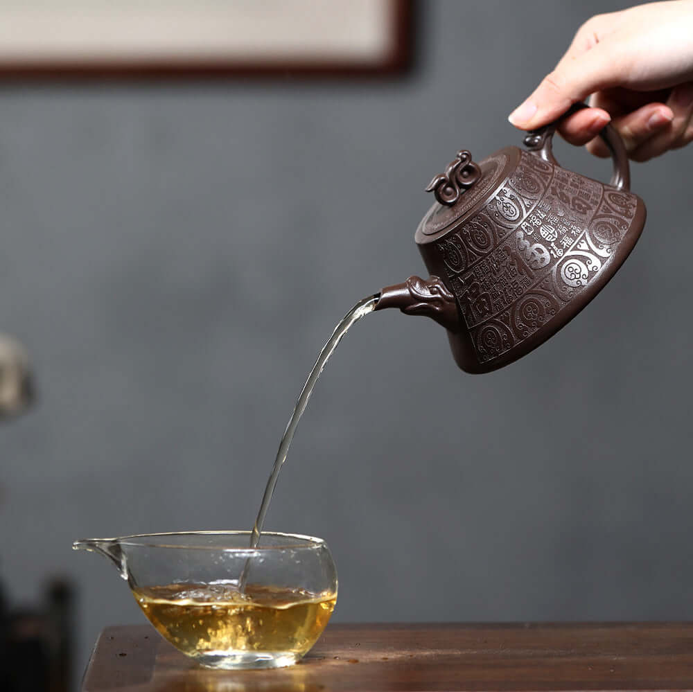Handmade Yixing purple sand teapot pouring tea into a glass cup, showcasing intricate craftsmanship.