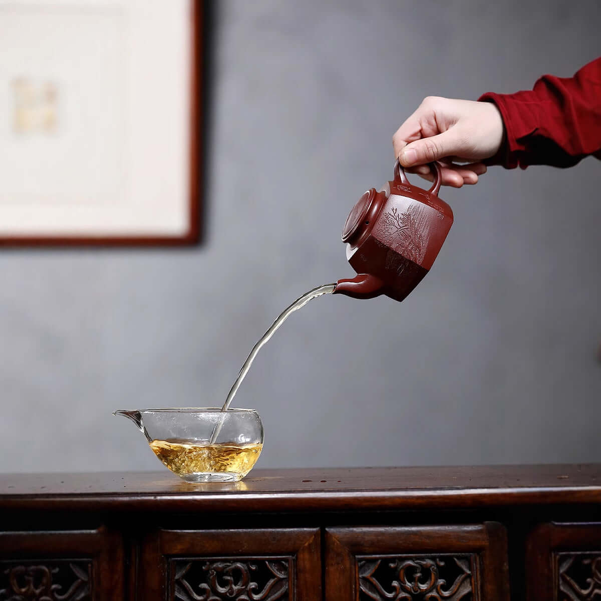 Handmade Yixing purple sand teapot pouring tea into a glass cup, showcasing traditional Chinese tea culture.