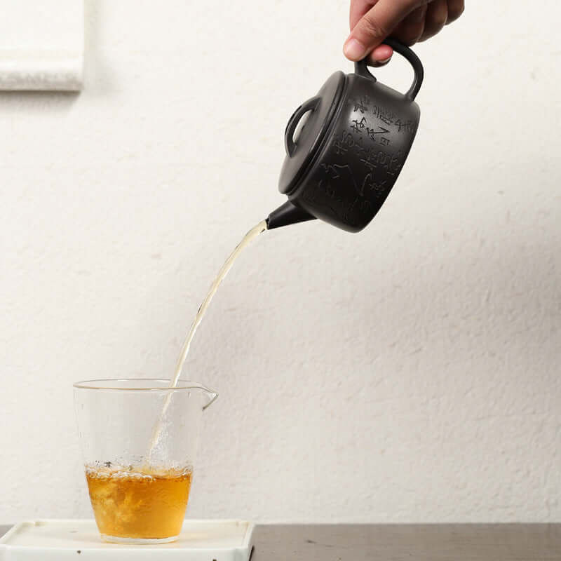 Handmade Yixing purple sand teapot pouring tea into a glass cup, showcasing elegance in Kung Fu tea ceremony.