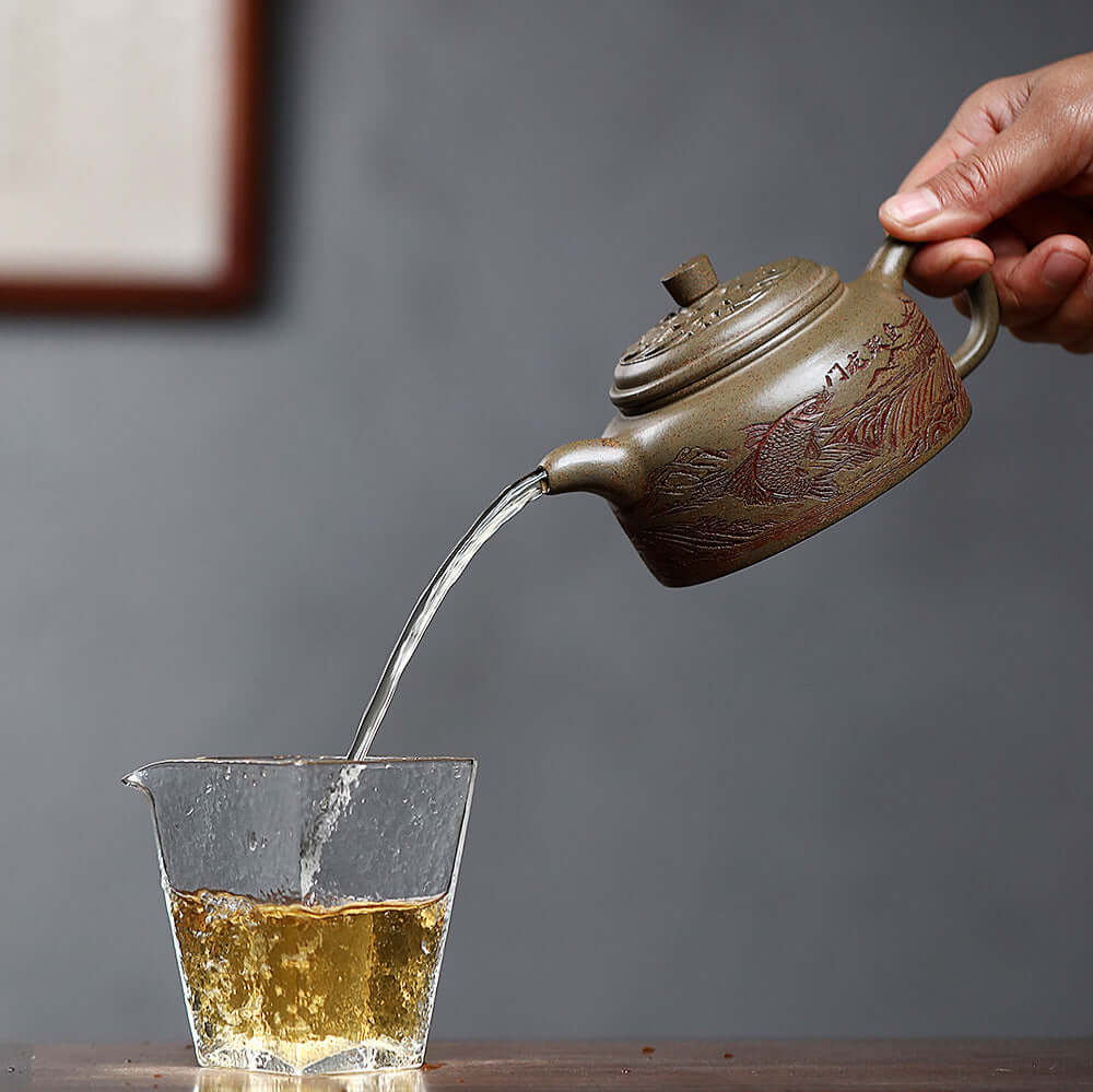 Handmade Yixing purple sand teapot pouring tea into a glass cup, showcasing craftsmanship and elegance in tea brewing.
