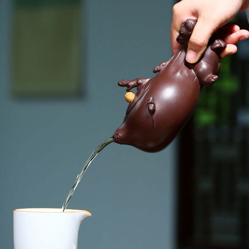 Handmade Yixing purple sand teapot pouring tea, featuring intricate detail of a mouse design.