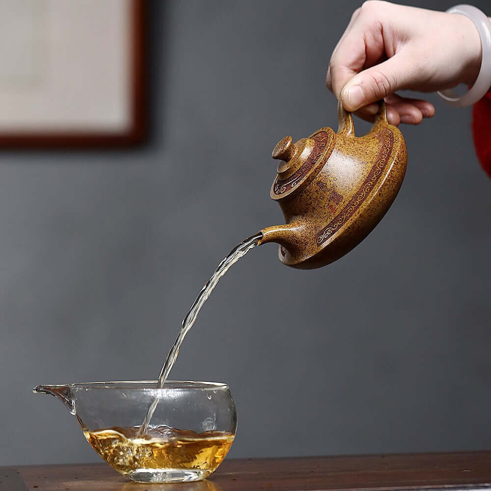 Handmade Yixing purple sand teapot pouring tea into a glass cup, showcasing traditional craftsmanship and design.