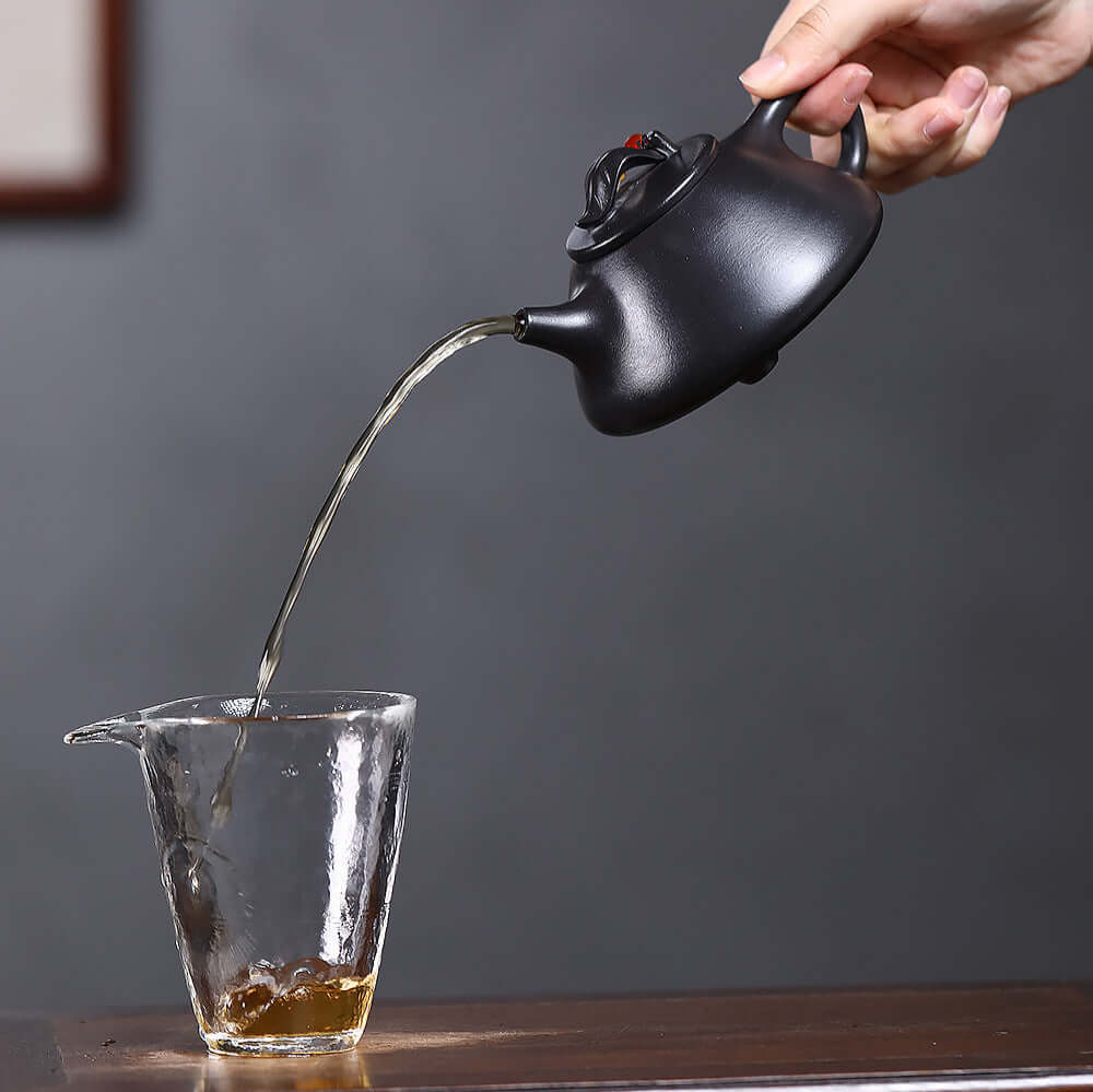 Handmade Yixing purple sand teapot pouring tea into a glass cup, showcasing traditional Kung Fu tea set craftsmanship.