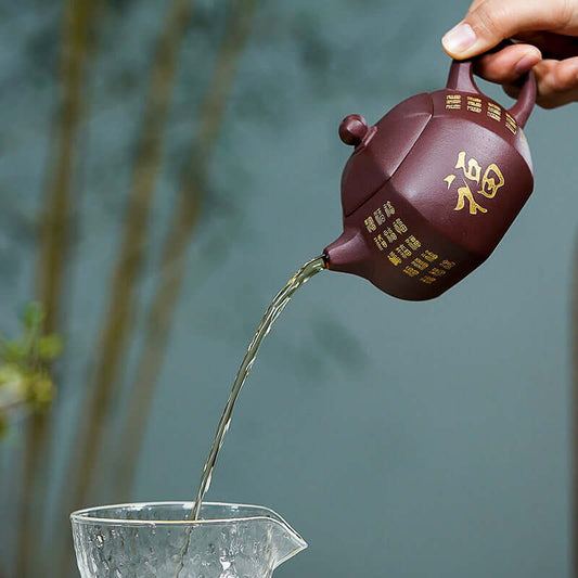 Handmade Yixing purple sand teapot pouring tea into a glass pitcher, showcasing intricate craftsmanship.