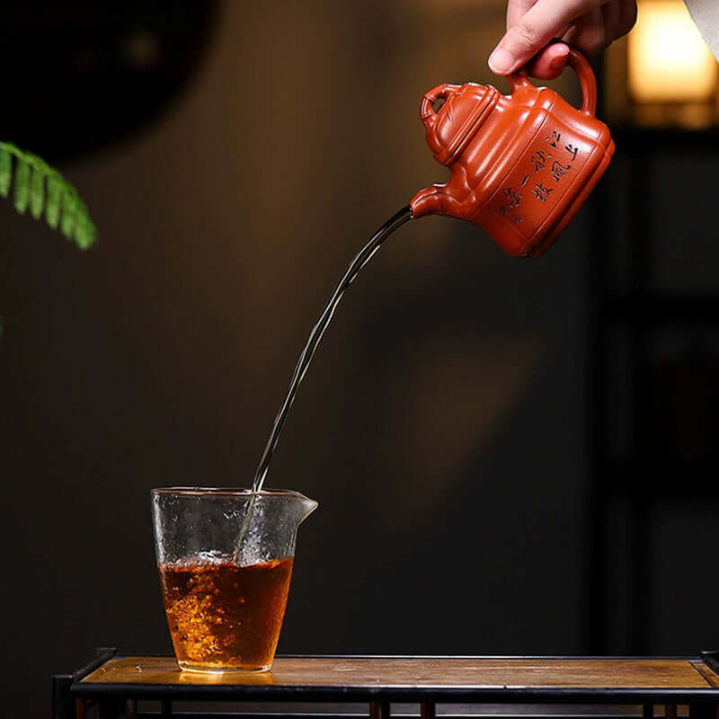 Handmade Yixing purple sand teapot pouring tea into a glass, showcasing traditional craftsmanship and vibrant color.