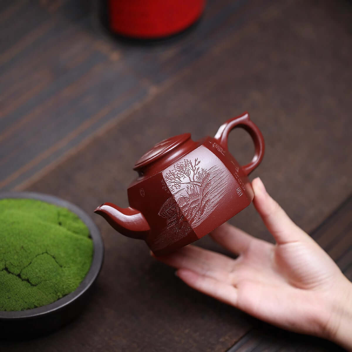 Handmade Yixing purple sand teapot with intricate design, held by a hand, ideal for kung fu tea ceremony.