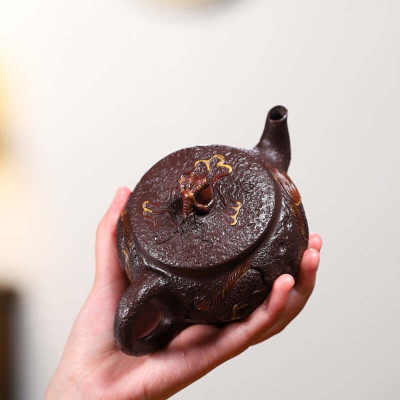 Handmade Yixing purple sand teapot featuring a dragon motif, held in hand, showcasing intricate design and craftsmanship.