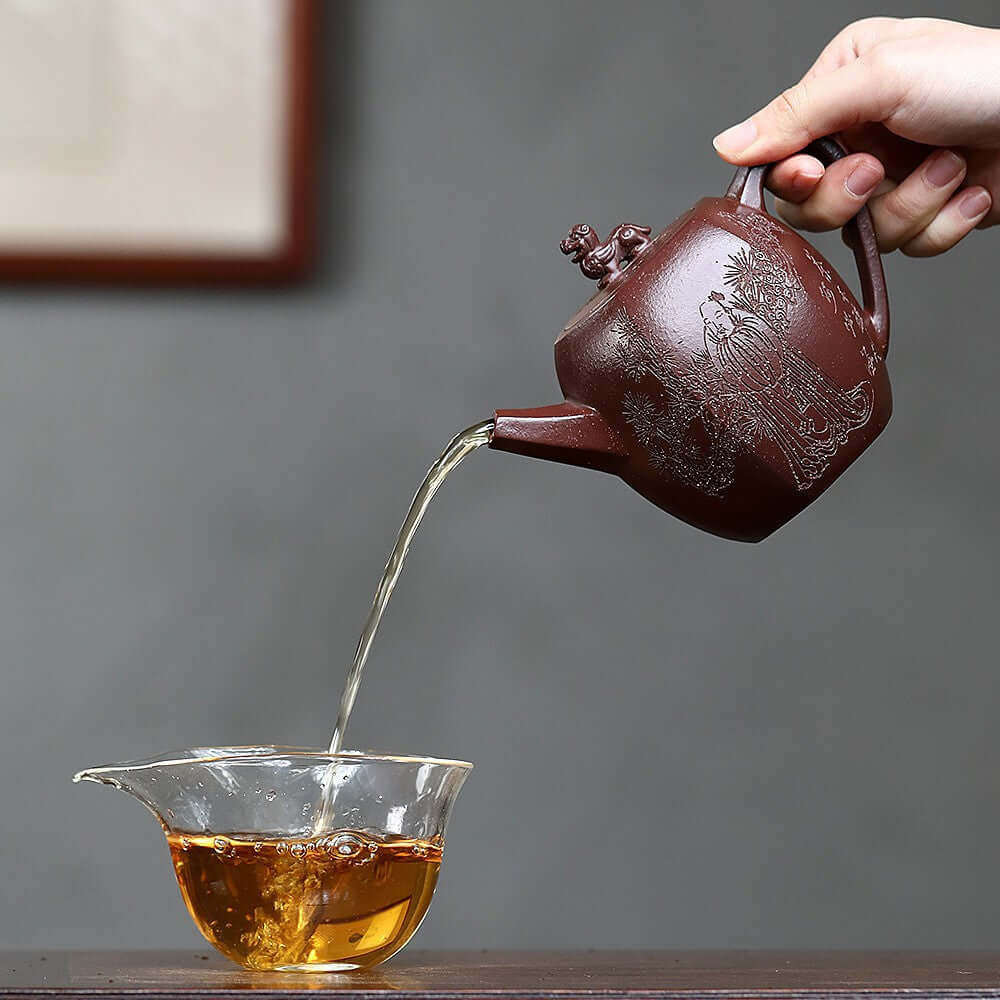 Handmade Yixing purple sand teapot pouring tea into a glass cup, showcasing traditional craftsmanship in tea ceremonies.