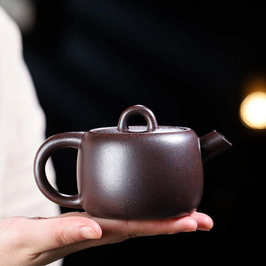 Handmade Yixing purple sand teapot held in hand, showcasing elegant design and craftsmanship.