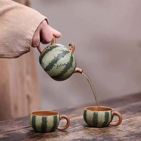 Handmade Yixing purple sand teapot pouring tea into two matching cups in a bionic watermelon design.