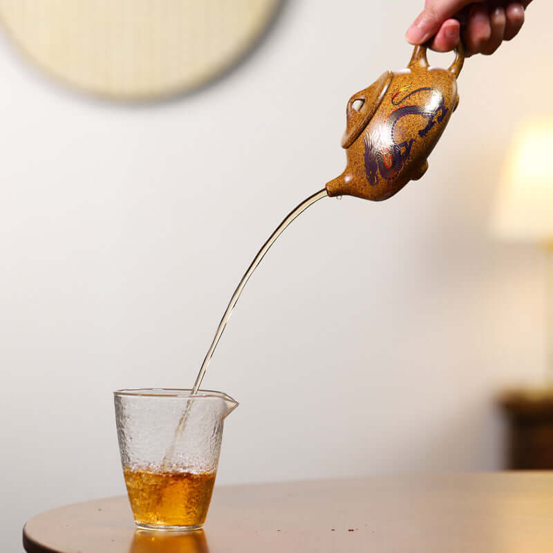 Handmade Yixing purple sand teapot pouring tea into a glass cup, showcasing its elegant design and craftsmanship.