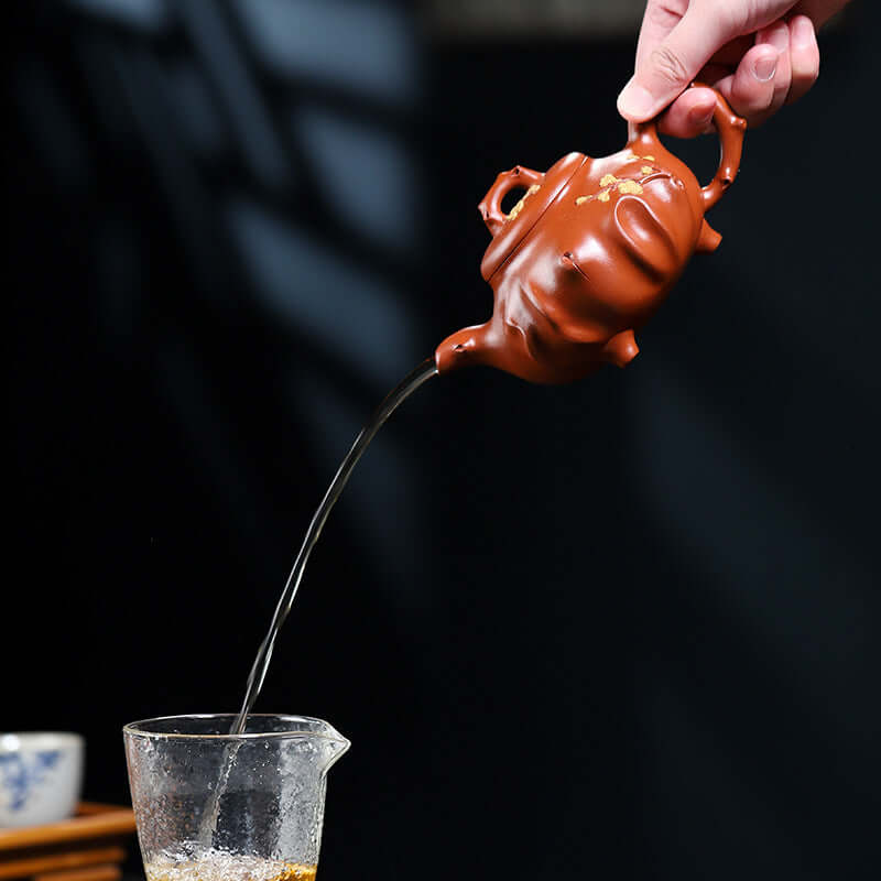 Handmade Yixing purple sand teapot, pouring tea from delicate spout into a glass cup.